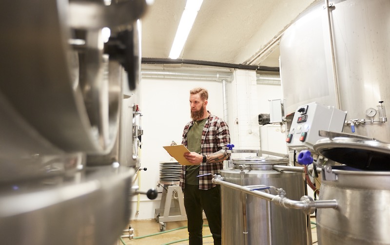 A man dressed in flannel inspects brewing equipment at small brewery