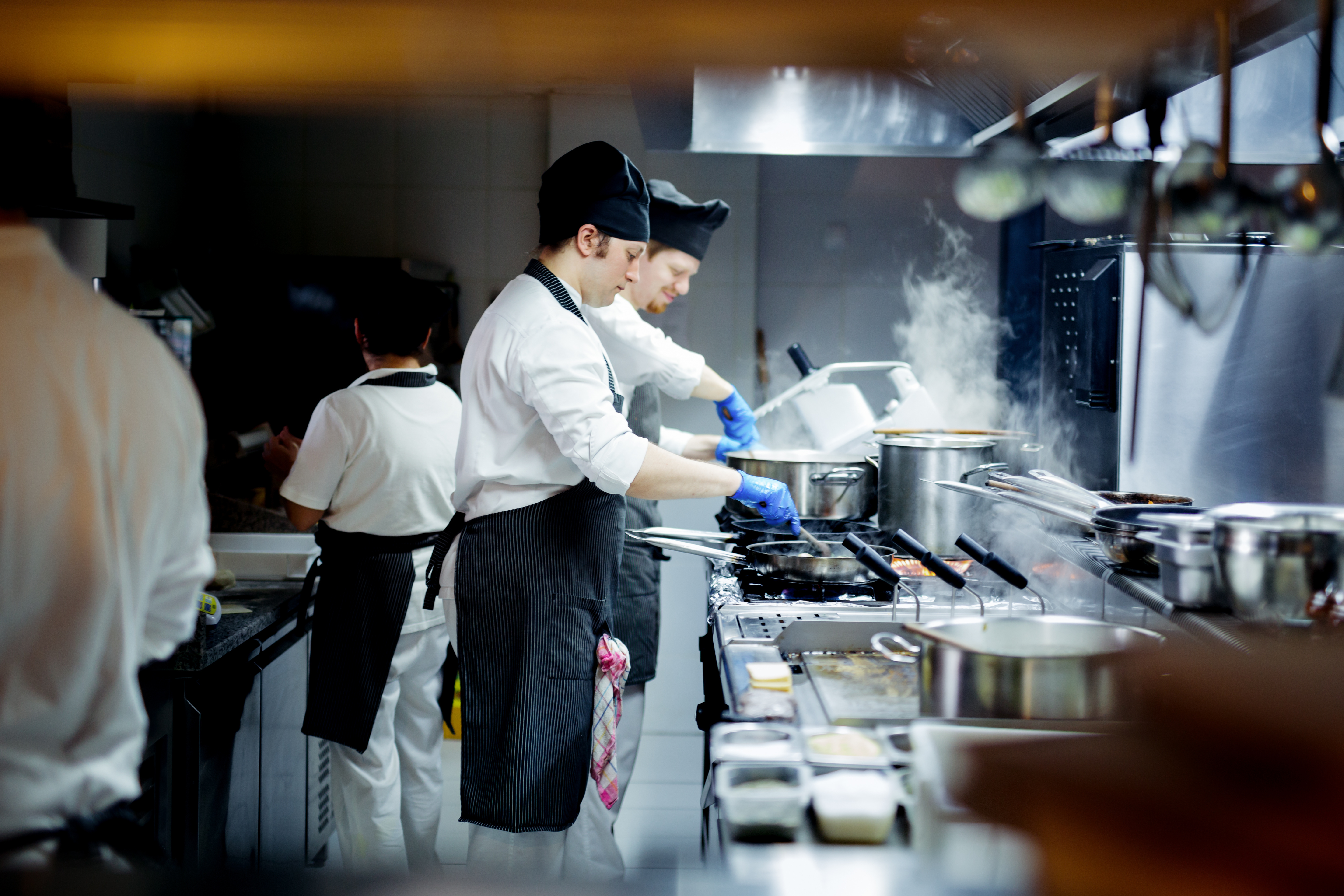 Chefs in a busy commercial restaurant kitchen with stainless steel equipment 
