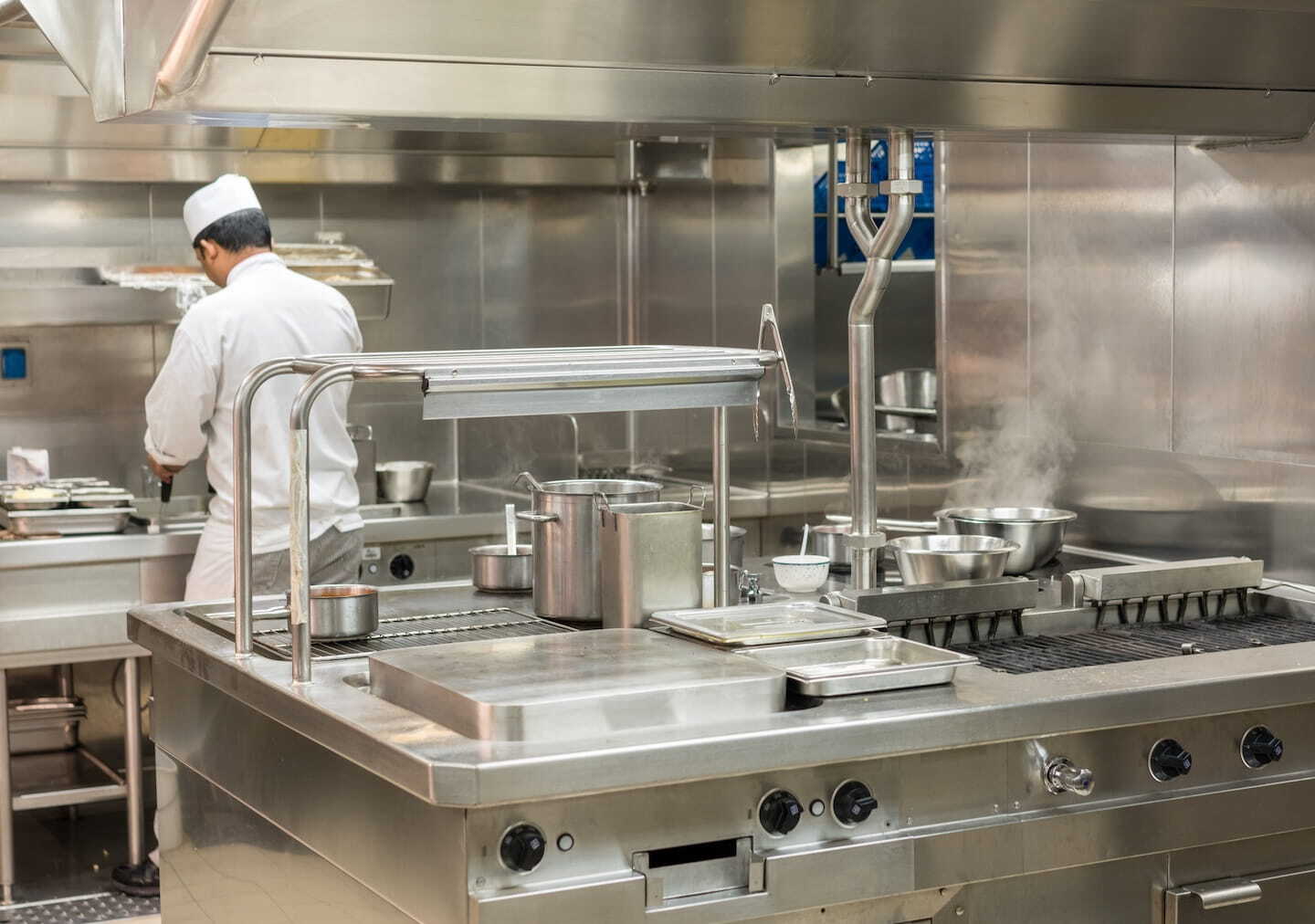 Stainless steel panel wall in commercial kitchen with worker cooking in background &ndash; Waterloo Paneling. 